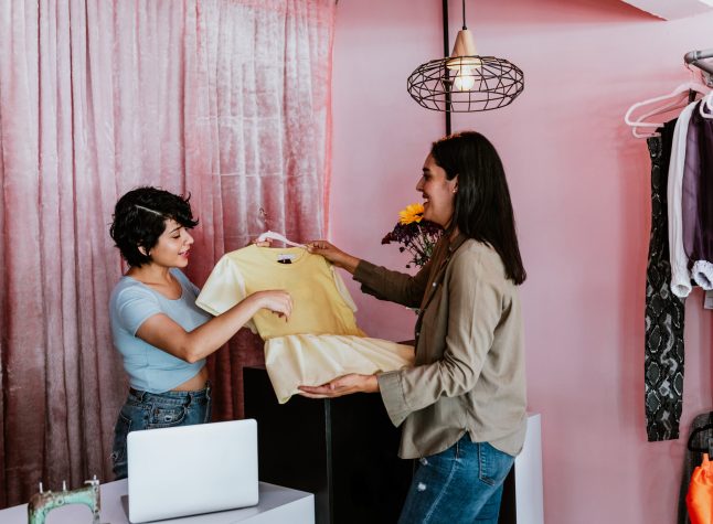 hispanic woman customer shopping in Clothing Store, Retail Sales Associate Assists Client in Fashionable Shop choosing Stylish Clothes, Colorful Brand Designs in Mexico Latin America