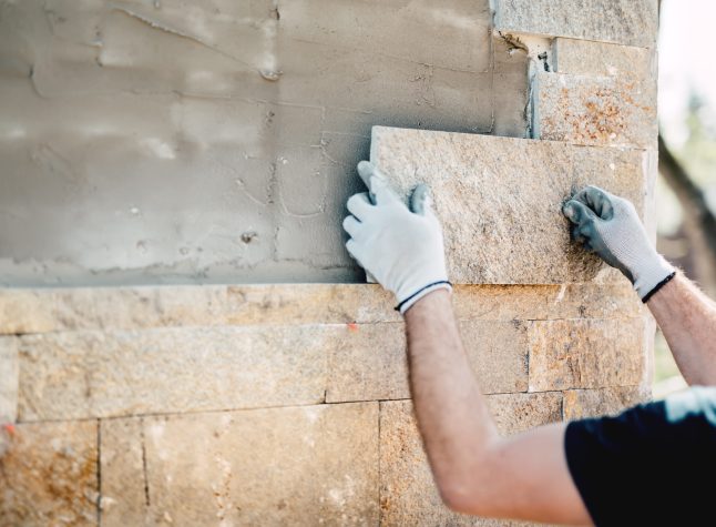 Construction worker installing stone on architectural facade of new building. details of construction industry