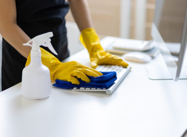 Young Asian cleaning woman uses a towel to clean a computer using cleaning solution in her home office.